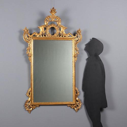 Carved and gilded wooden mirror. The frame is embellished with leaf and floral carvings, as well as Rocaille-style scrolls...