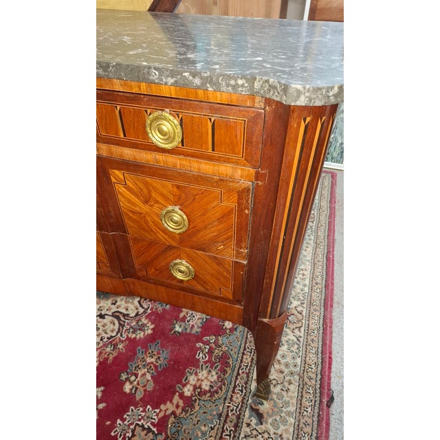 A louis xv/xvi transitional marquetry commode with a marble top. This commode rests on three drawers. It is decorated with...