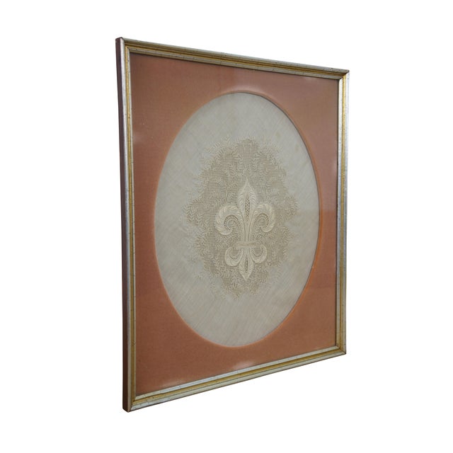 Antique framed piece of intricate lace and embroidery on white linen depicting a French fleur de lis surrounded swirling...
