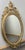 This Vintage French oval wall mirror is richly decorated with classical scrollwork and an elegant urn-and-floral crest,...