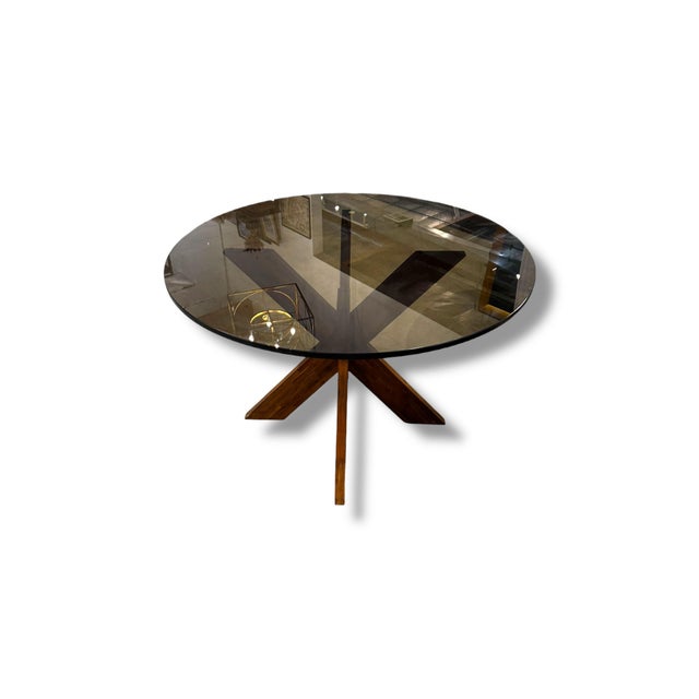 Striking mid century modern dining table featuring a large round smoked glass top paired with a sculptural crossed wood...