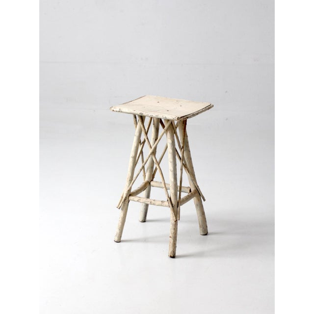 Antique Adirondack twig side table featuring a naturally sculptural branch frame, square plank top, and weathered painted...