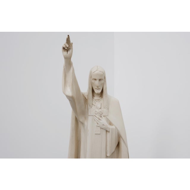 This devotional plaster statue depicts christ the king, standing with one hand raised in blessing and the other pointing...