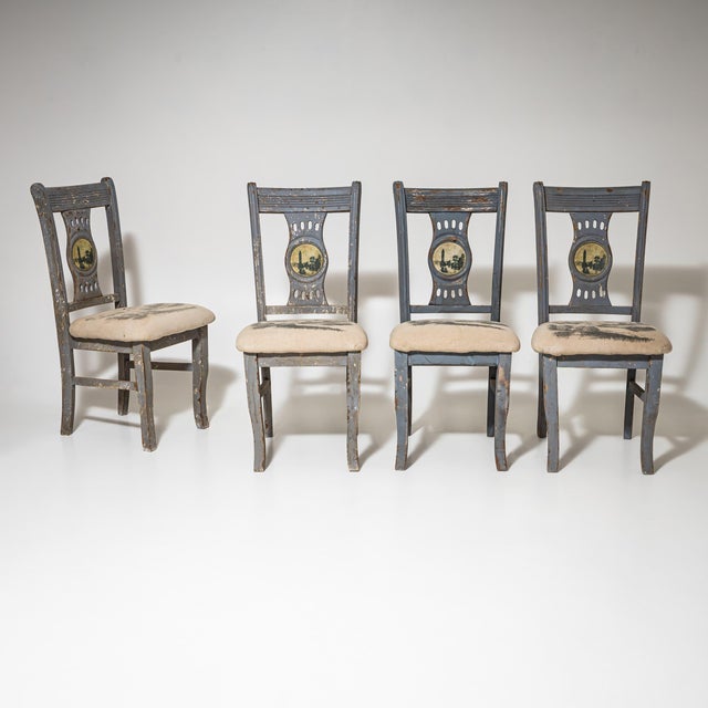 Set of four gray painted side chairs with upholstered seats. The central splat of each backrest is decorated with a...
