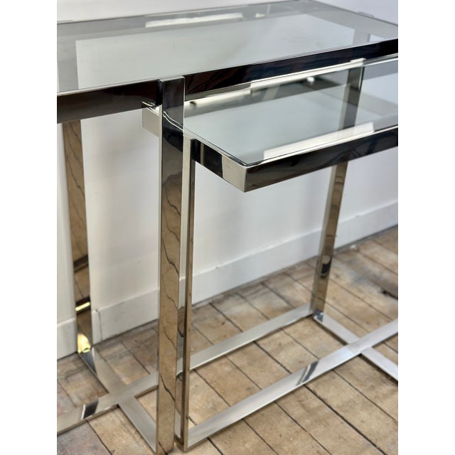 Double console table in chromed metal with clear glass tops, dating from the 2000s. Its minimalist, architectural design...