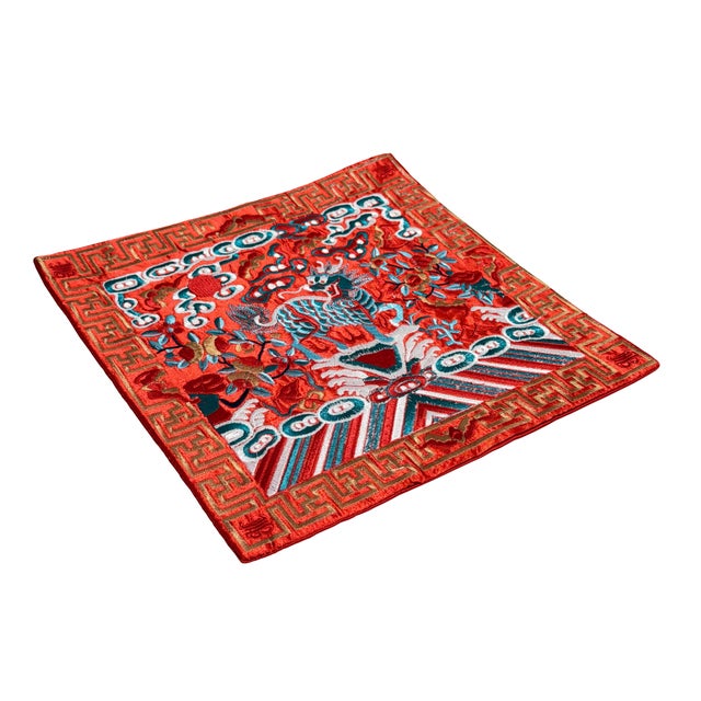 This striking, finely embroidered square textile panel features a vibrant red background richly detailed with traditional...