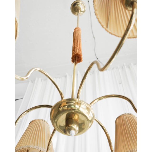 This mid-century chandelier, likely from France, features a brass frame and six arms. Elegant shades are positioned...