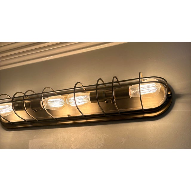 Industrial modern. 28” x 7”. 4 bulbs in cage. Warm brushed brass/bronze. Leans class is without feeling rustic Curved bars...