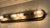 Industrial modern. 28” x 7”. 4 bulbs in cage. Warm brushed brass/bronze. Leans class is without feeling rustic Curved bars...