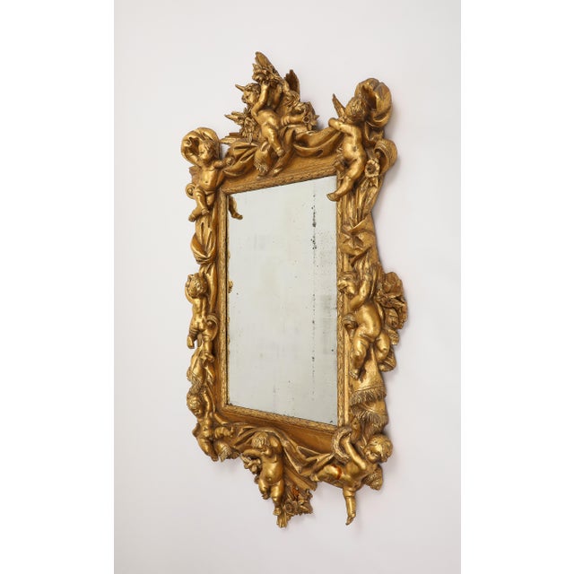 20th century Italian Baroque style giltwood mirror, ornamented with florals and cherubs along a carved drapery border....