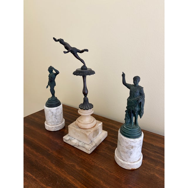 A refined collection of Grand Tour–style metal figures mounted on richly varied marble bases, each piece evoking the...
