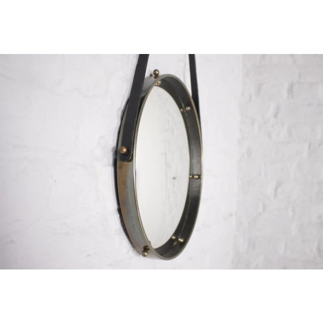 Suspended convex mirror, the frame crossed by solid brass balls, suspended by a black leather belt. In the style of...