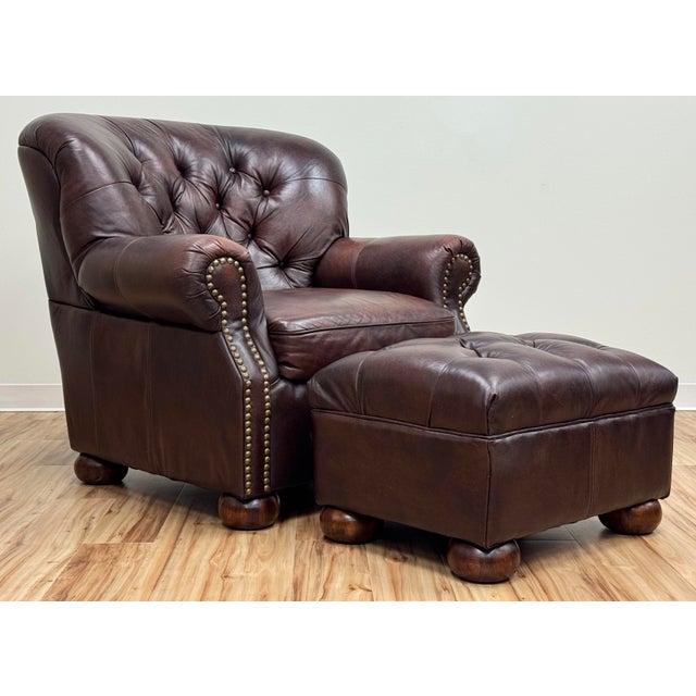Classic vintage tufted wingback chair and ottoman upholstered in a warm brown leather. Features deep button tufting on the...
