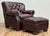 Classic vintage tufted wingback chair and ottoman upholstered in a warm brown leather. Features deep button tufting on the...