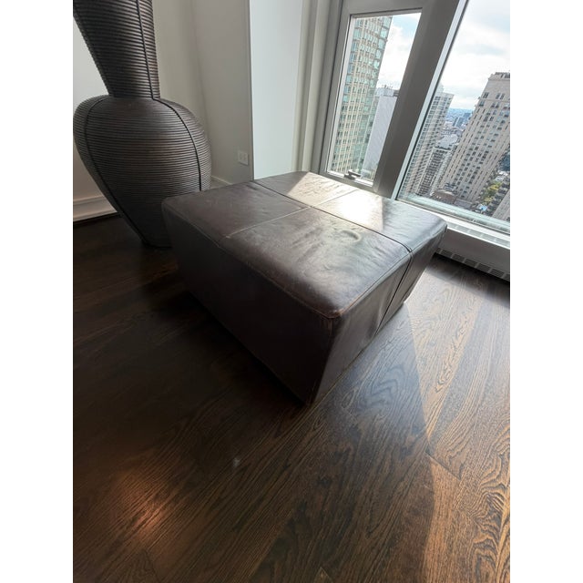 A sleek Room & Board square leather ottoman featuring rich espresso leather upholstery and clean, modern lines. The...