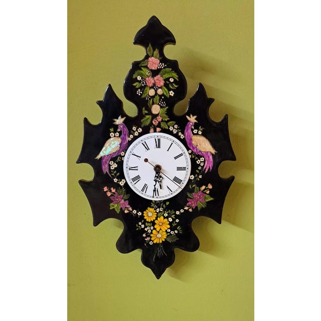 A handcrafted wall clock, lacquered in black and meticulously decorated with hand-painted flowers and exotic birds...