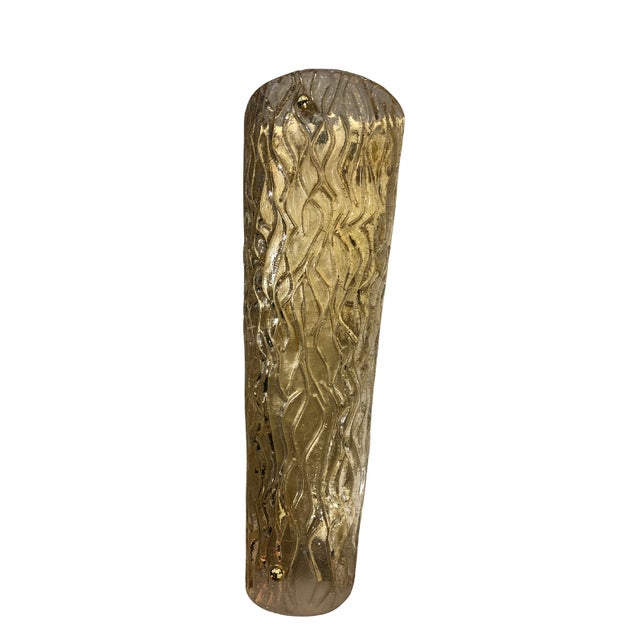 This piece features an elongated cylindrical design crafted from Murano glass with a golden amber hue. The organic, fluid...
