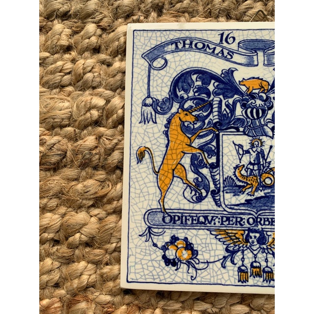 A classic Dutch Delft-style hand painted blue and white porcelain tile featuring an intricately rendered heraldic coat of...