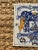 A classic Dutch Delft-style hand painted blue and white porcelain tile featuring an intricately rendered heraldic coat of...