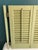 This vintage pair of wooden shutters features traditional louvered panels finished in a soft green paint with a naturally...
