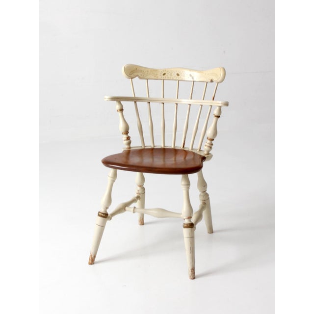A vintage Ethan Allen comb back chair featuring a classic American silhouette with a warm wood seat and a cream painted...