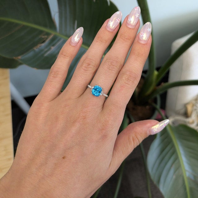 A Cambodian blue zircon blazes with extraordinary brilliance in this elongated cushion ring, accented with diamonds in...
