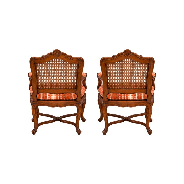 A charming pair of wood armchairs featuring shaped frames, woven cane backs, and tailored tangerine-striped seats. The...