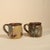 This charming pair of handmade studio pottery mugs showcases warm earth-toned glazes, subtle painterly floral accents, and...