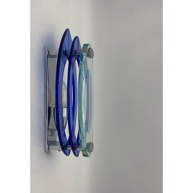 Modern design wall light featuring a chromed metal frame and a diffuser composed of three overlapping oval glass elements,...