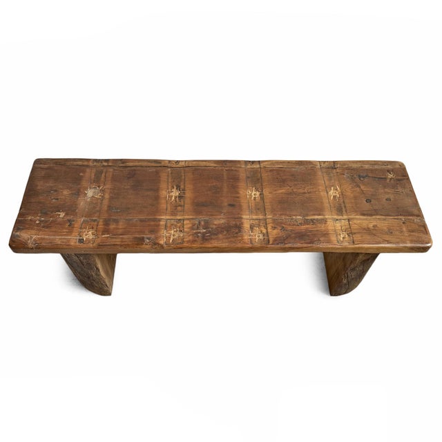 Vintage solid wood bench with cut log legs and old wood panel used as a seat. Indents and markings on panel are present...