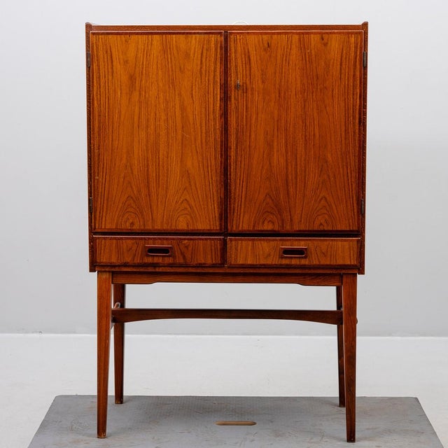 Swedish bar cabinet, ca 1960-65, in rosewood veneer and teak. A freestanding cabinet on slender legs, featuring two doors,...