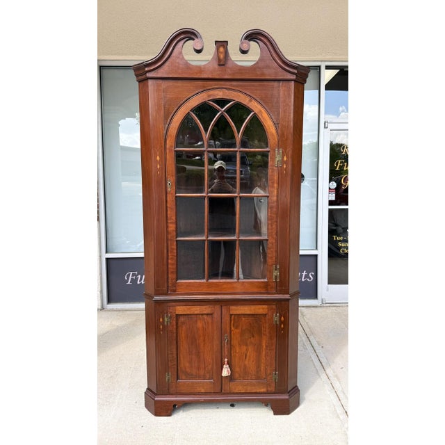 This 18th Century Inlaid Mahogany Corner Cabinet features an elegant arched glass door, graceful scroll pediment, and...