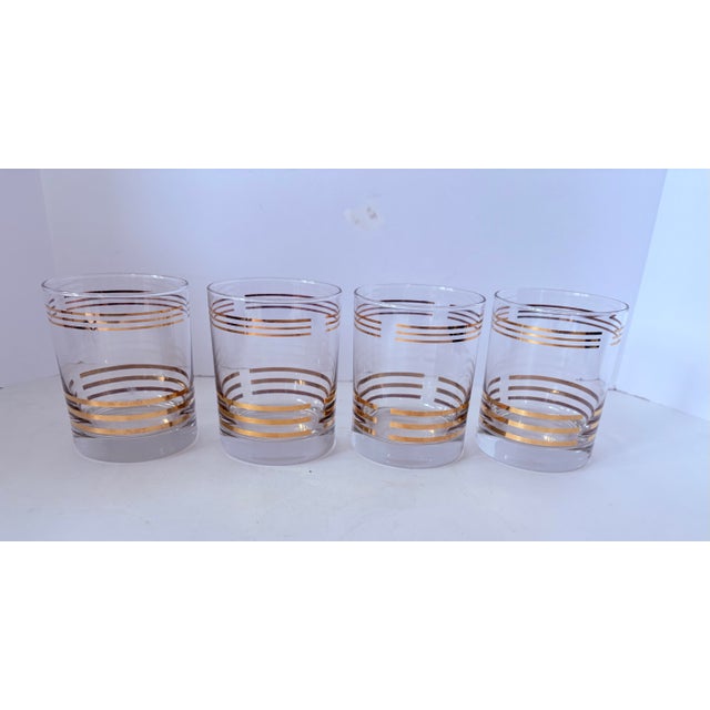 A refined set of four mid-century rocks glasses featuring elegant gold banding and clean, architectural lines. These...