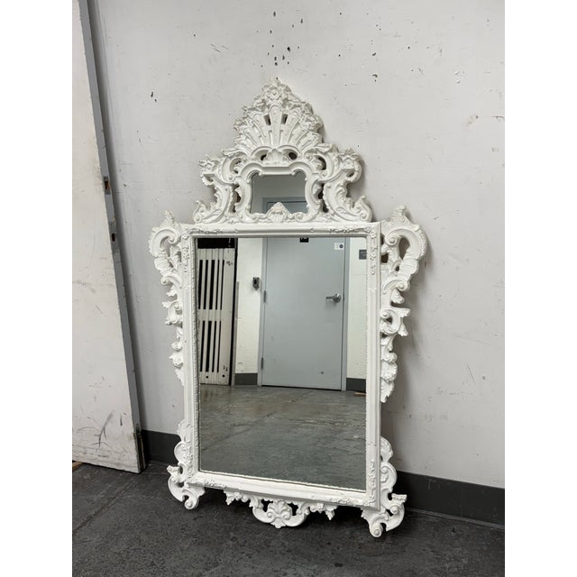 Design Plus Gallery presents a Circa 1970 Hollywood Regency Wall Mirror. The mirror has an ornate molded frame in white...