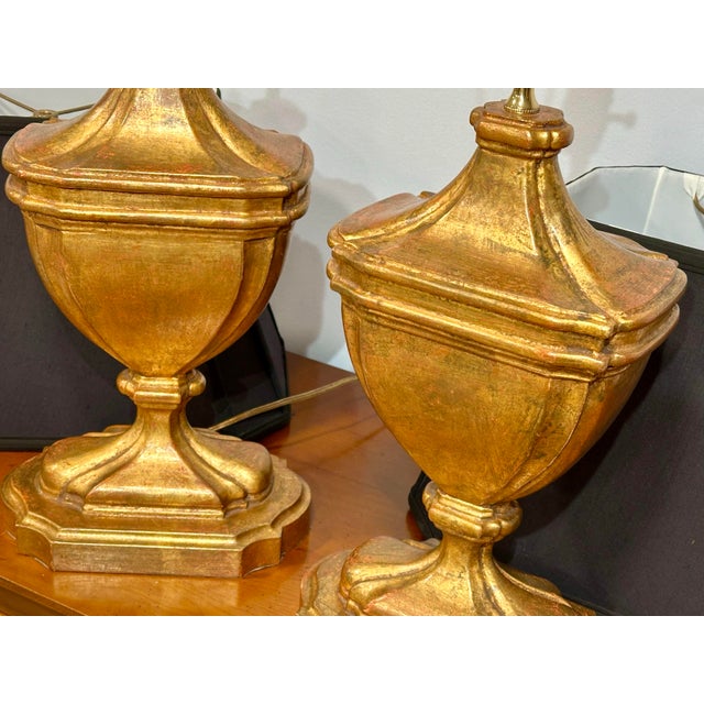 A handsome pair of carved wood urn-form table lamps featuring an antiqued gilt or distressed gold leaf finish with...