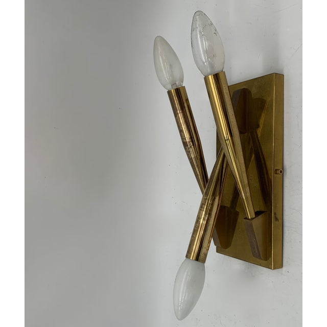 A pair of large and small brass wall sconces with a refined modernist design, comprising a three-light and a four-light...