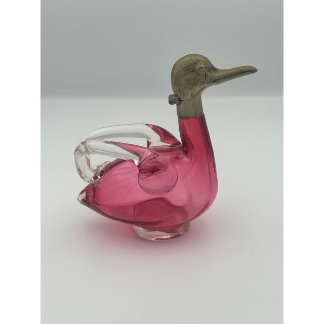 A sculptural mid‑century Czech art glass duck‑form decanter featuring a vibrant pink blown‑glass body with clear applied...