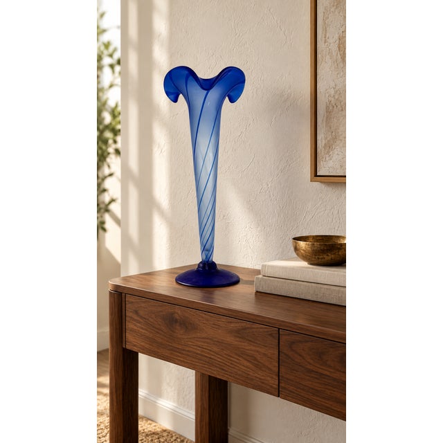 A sculptural glass vase featuring a slender, tapered silhouette and a dramatically flared, ruffled opening. Dark blue...