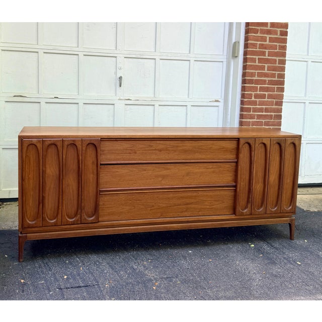 Gorgeous sculptural walnut dresser featuring a stunning sculptural design, adorned with three spacious central drawers...