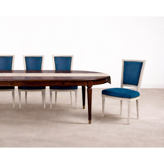 A refined set of eight mid-20th century French dining chairs featuring painted ivory frames and patterned peacock-blue...
