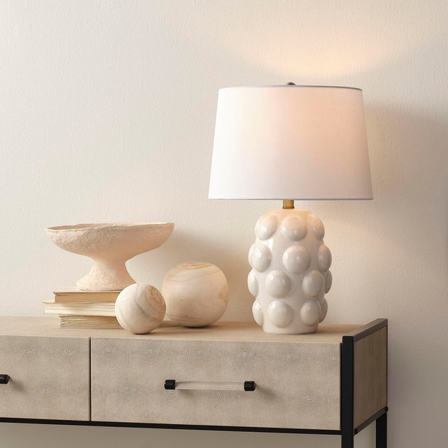 Texture takes center stage in this white-on-white table lamp, featuring a cream ceramic body adorned with a hand-applied...