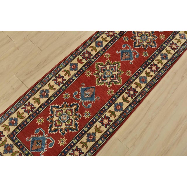 A tribal Caucasian Kazak runner hand-knotted with fine wool on a cotton foundation. This rug features geometric medallions...