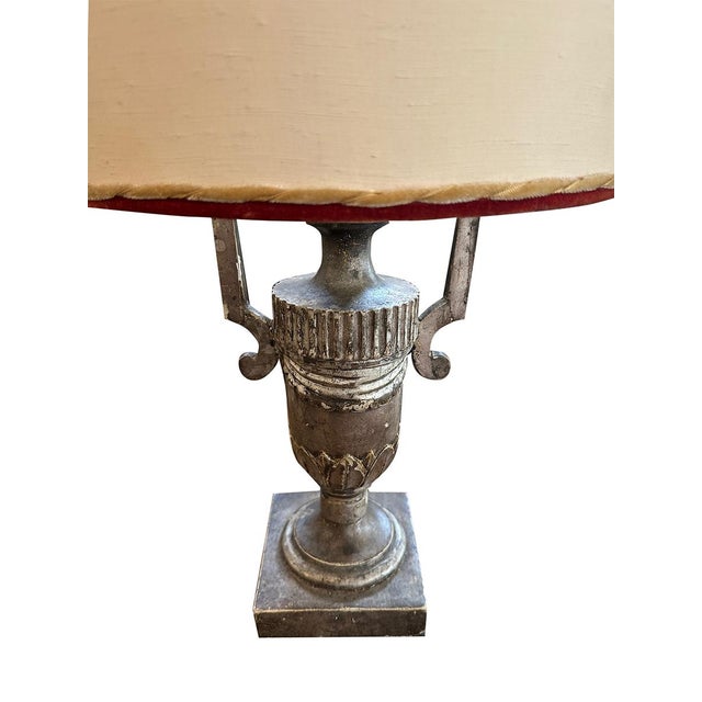 This pair of urn lamps has a base of wood, painted silver. The shade have gold cord and red borders. These matching lamps...