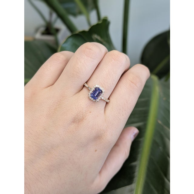 A vivid 1-carat emerald cut tanzanite takes center stage in this breathtaking ring, framed by a halo of sparkling earth-...