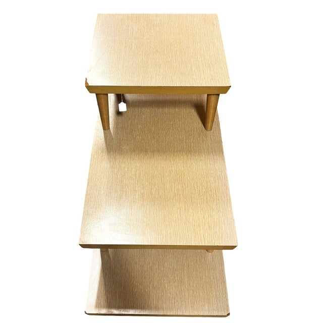 Rare Mid-Century Modern blonde laminate three tier side tables with brass ferrule tapered legs. The tabletop surfaces are...