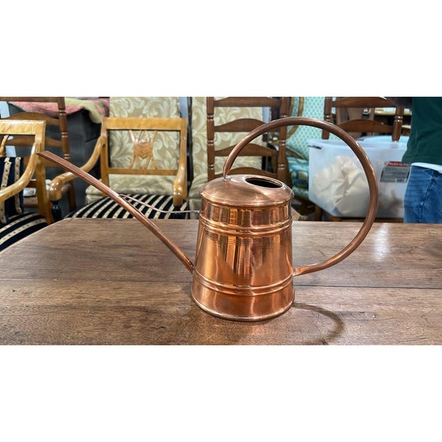 An elegant vintage copper watering can featuring a polished finish with subtle ridged band accents along the tapered...
