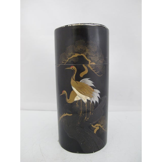 The tin is most likely a vintage Japanese tea caddy with double lid. Decorated with a black and gold lacquer-style crane...