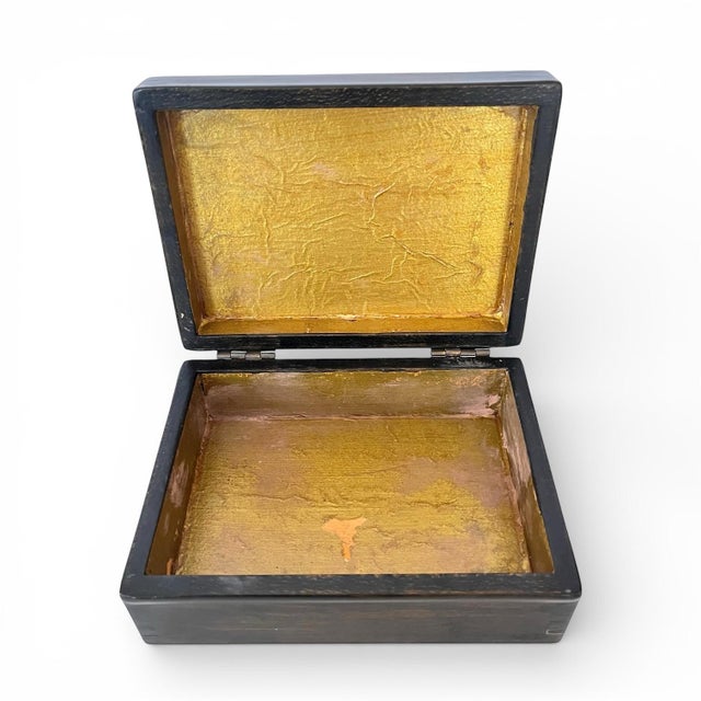A vintage ebonized wood box featuring a detailed nautical scene on the lid of a sailboat fleet, with textured gold foil...