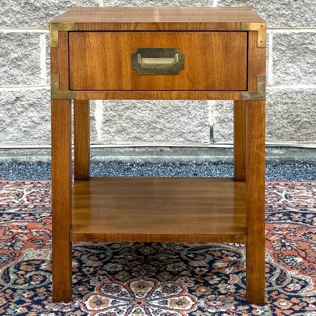 A vintage Dixie Campaigner collection pecan and brass nightstand having one dovetailed drawer over block legs and an open...