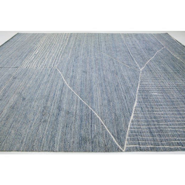 This luxurious wool rug features a timeless Moroccan pattern in a contemporary abstract Minimalist style, utilizing blue...